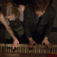 Starbuck (Katee Sackhoff) and a stranger (Roark Critchlow) play "All Along the Watchtower" on a piano in Battlestar Galactica.